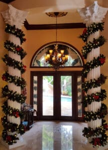 Interior entryway columns wrapped with Christmas garland, red bows, and warm white lights installed by Christmas Decor in Boynton Beach